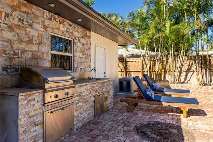 Stone outdoor kitchen island with a grill, sink and cabinets beside a patio