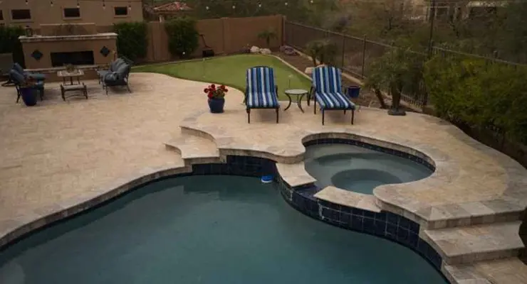Travertine pool deck with a spa and two lounge chairs