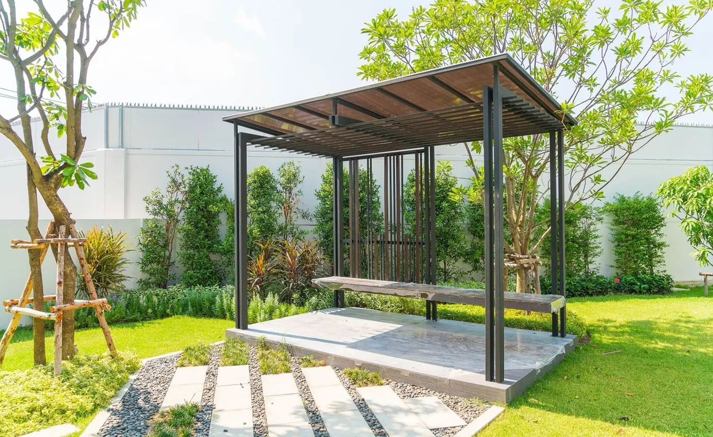 Dark-framed pergola with a wood roof over a stone platform in a garden
