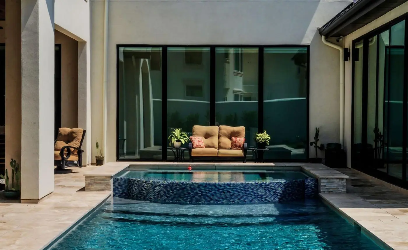 Courtyard residential pool with a tiled raised spa and outdoor sofa beside glass doors