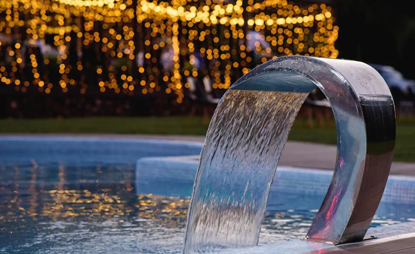 Stainless steel pool water feature spilling into a lit pool by Heavenly Outdoor in Richmond, TX